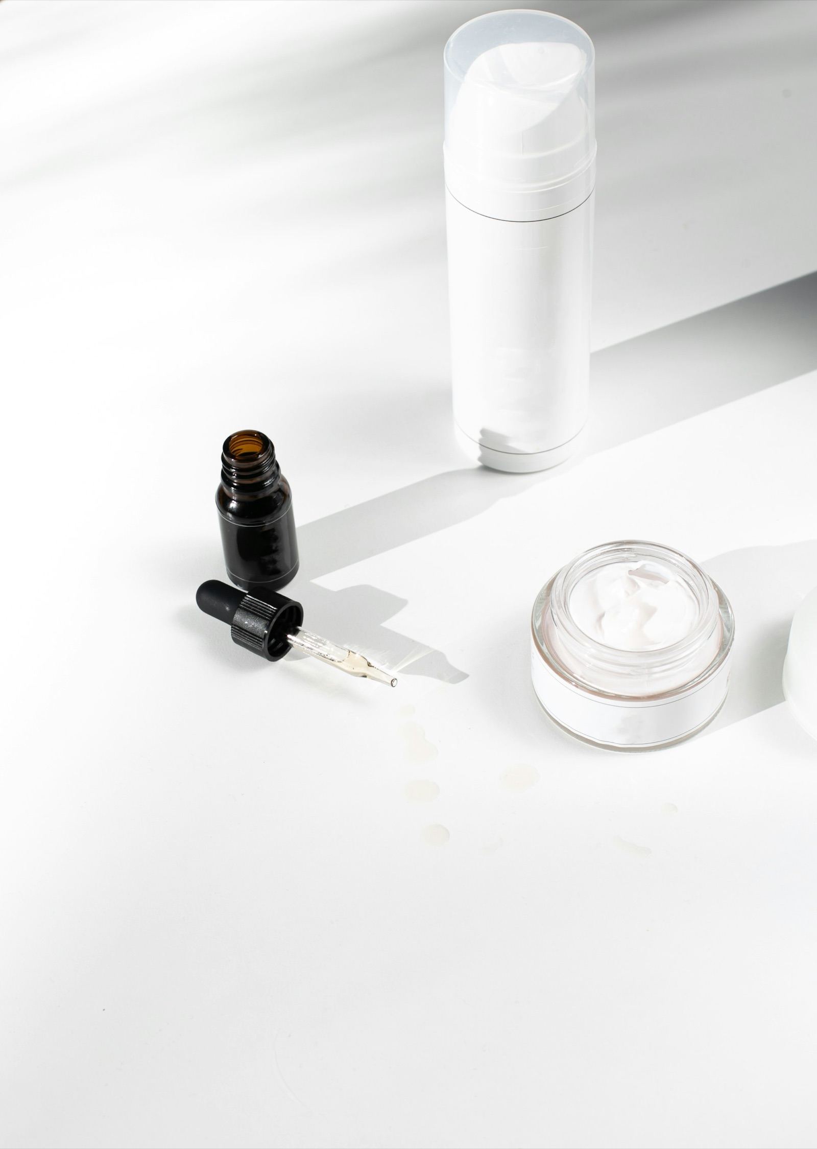 A skincare dropper and jar in white light
